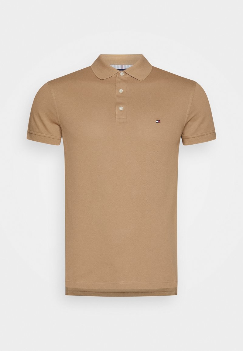 Polo shirt en coton marron avec un col classique, trois boutons, des manches courtes et un petit logo sur la poitrine gauche. Texture lisse.