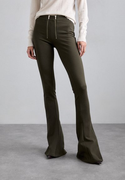 Pantalons évasés verts olive avec deux poches zippées à la taille, fabriqués dans un matériau lisse et extensible, présentant des coutures propres et une coupe ajustée.