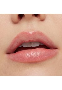 Nahaufnahme von Lippen mit einem sanften Rosaton. Glatte Textur, leicht pralles Format und ein natürlicher Glanz. Zähne sind teilweise sichtbar.