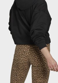 Sudadera negra corta con capucha ajustable, combinada con pantalones ajustados de leopardo marrón, que destacan por su textura y un patrón animal prominente.