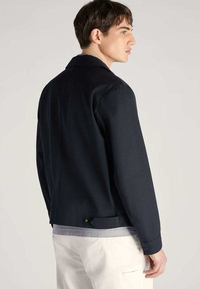 Marynarka w kolorze navy o gładkiej fakturze, dopasowanym kroju, lekko skróconym fasonie i kołnierzu w kształcie punktu. Posiada subtelny złoty akcent w pobliżu dołu.