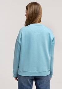 Jasnoniebieska bluza o luźnym kroju, z ribbowanym dekoltem i mankietami. Gładka faktura, prosty design i opadające szwy na ramionach.