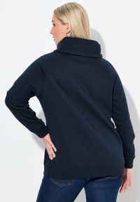 Sudadera azul marino con un cuello alto y doblado y puños acanalados. Fabricada en un material suave, presenta un corte holgado y detalles de costura.