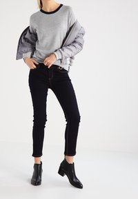 Sudadera gris con cuello azul marino, combinada con vaqueros pitillo negros con costuras en contraste y botines negros con tacón.