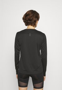 Schwarzes Langarmshirt aus glattem Stoff, mit rundem Ausschnitt und einer Reihe kleiner weißer Punkten am oberen Rücken.