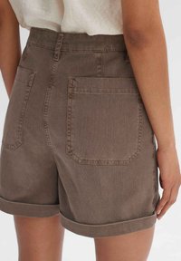 Bruine denim shorts met een hoge taille, opgerolde boorden en twee grote achterzakken. De stof heeft een subtiele textuur.