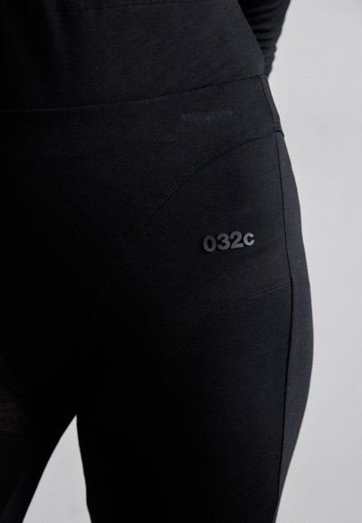 Black leggings made from stretchy fabric. Features a smooth texture, flat seams, and a small embossed logo "032c" on the thigh.