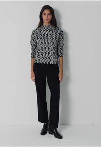 Schwarzer und weißer gemusterter Pullover mit hohem Ausschnitt, Dreiviertelärmel, kombiniert mit schwarzen geraden Hosen und Knöchelstiefeln.