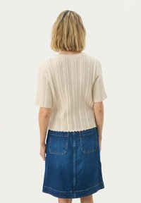 Pull en maille crème à manches courtes avec un motif texturé en côtes ; associé à une jupe en denim bleu foncé comprenant deux poches arrière.