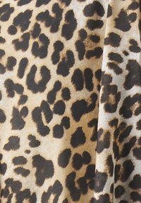 Tela de estampado de leopardo con manchas marrones y negras sobre un fondo beige claro. La textura parece suave con un ligero brillo.