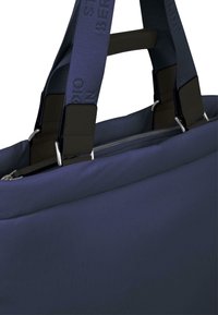 Mørkeblå duffelbag med polstret stof, dobbelte håndtag, teksturerte stropper og sølvfarge detaljer. Med glidelås på toppen for enkel tilgang.