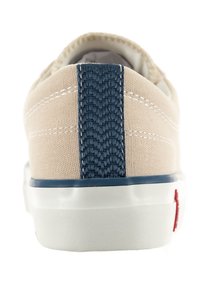 Zapatilla de lona beige con un acento en el talón texturizado en color marino, costuras blancas y una suela de goma blanca con un logo rojo.