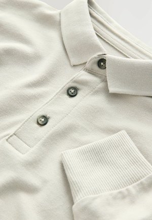 Ljusbeige polo-shirt med texturerad tyg, traditionell krage, tre knappar och ett ribbat ficka.