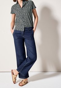 Zwart-wit patroon overhemd met korte mouwen, blauwe wijde jeans met contrasterende stiksels, gecombineerd met lichtbruine gevlochten sandalen.