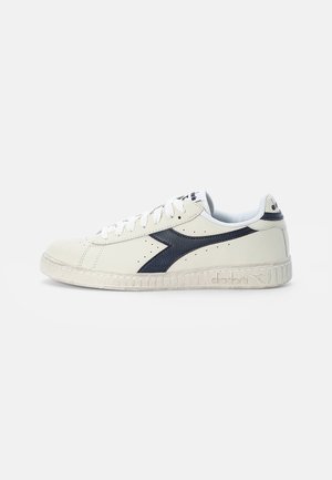 Sneaker in pelle bianca con dettagli blu navy, punta tonda, suola in gomma testurizzata e lati perforati. Presenta lacci bianchi e dettaglio del logo.