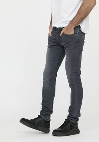 Dunkelgraue Slim-Fit-Jeans mit glatter Textur, fünf Taschen und klassischem Design, kombiniert mit schwarzen Sneakers.