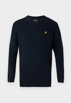Marineblå v-hals genser laget av mykt stoff, med lange ermer og en liten gul brodert logo på venstre bryst.