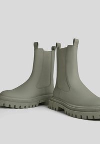 Zielone gumowe botki Chelsea z elastycznymi panelami bocznymi, teksturowanymi podeszwami i uchwytami. Gładkie wykończenie i masywny design zapewniający dodatkową stabilność.