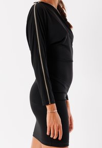 Abito nero realizzato in tessuto elasticizzato, con un design aderente, maniche lunghe e un dettaglio di zip laterale argentata. Texture morbida.