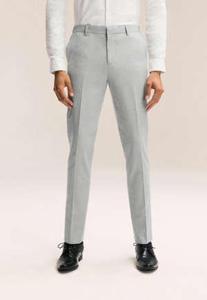 Pantalones gris claro a medida, confeccionados con una tela suave, con un diseño de pierna recta, presillas para cinturón y bolsillos laterales, combinados con zapatos negros.