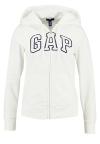 Sudadera blanca con cremallera y bolsillos frontales, con el logo "GAP" en grandes letras azules marinas contorneadas en el pecho.