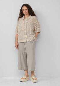 Chemise à rayures beige à manches courtes avec des boutons sur le devant et deux poches, associée à un pantalon large gris clair et à des sandales plateforme beiges épaisses.