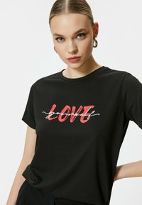 Camiseta de algodón negra con la palabra "LOVE" en letras rojas y en negrita en el frente, con "yourself" en cursiva blanca debajo, de cuello redondo.
