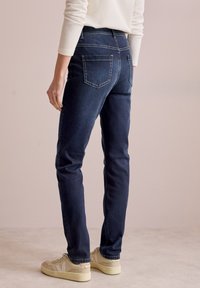 Mörkblå jeans i denim med rak passform, bakfickor och kontrasterande vit sömnad. I kombination med ljusa sneakers.