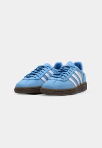 Blå mockasneakers med vita ränder, rund tådesign, platt brun gummisula och blå snörningsdetaljer.