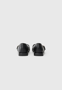 Mocassini in pelle nera con tacco basso, caratterizzati da una texture liscia e un design minimalista. La vista posteriore mette in risalto linee pulite e dettagli di cucitura.