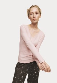 Top de punto acanalado de manga larga en rosa claro con escote en V y detalle de botones, combinado con pantalones oscuros con un patrón de estrellas.