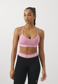 Sujeción deportiva rosa con tirantes finos, que presenta una banda elástica con marca. Combinada con leggings negros, que resaltan una textura suave y ajustada.