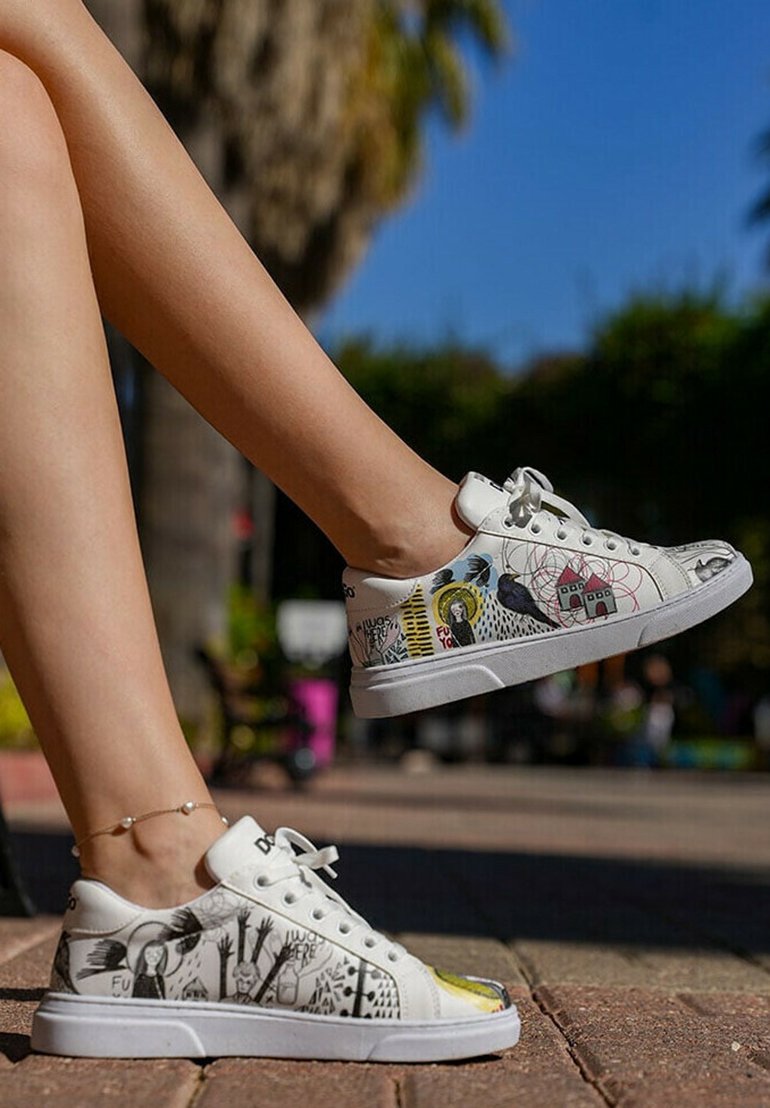 White sneakers with various graphic prints, including animals and text. Lace-up design, smooth leather material, and flat rubber sole.
