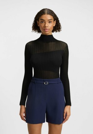 Un shirt à col roulé noir côtelé avec des sections transparentes, associé à un short taille haute bleu marine avec une ceinture et un accent en anneau.