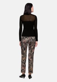 Black long-sleeve top with a sheer back, paired with floral-patterned pants featuring hues of pink and black. Footwear is black with a slight heel.