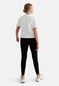 Vit bomull T-shirt och svarta leggings, åtsittande design, mjuk textur, bärs med vita sneakers. Utsikten visar baksidan av outfiten.