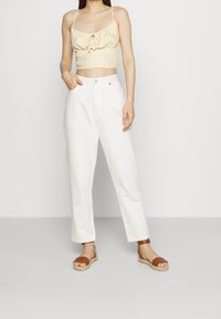 Yellow gingham crop top with ruffled detail, high-waisted light beige pants, and brown strappy sandals with a woven sole. Simple and casual outfit.