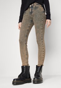 Jeans skinny de mezclilla marrón desvanecidos con cintura alta, dobladillo deshilachado, bolsillos frontales y costura en contraste, llevados con botas de combate negras.