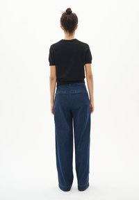 Schwarzes kurzärmliges Oberteil, kombiniert mit dunkelblauen, hoch taillierten, weit geschnittenen Jeans. Die Jeans verfügen über Gesäßtaschen und einen Saum mit sichtbaren Nähten.