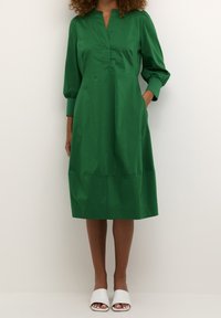 Grön bomullsklänning med V-ringning, knappdetaljer och trekvartslånga puffärmar. Har sidfickor och en lös passform.