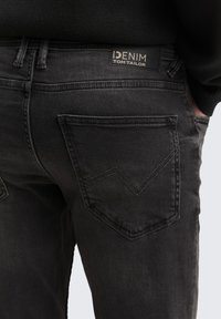 Čierne denimu nohavice so slim fit strihom, ktoré majú charakteristický V-šev vzor na zadných vreckách a značkový kožený štítok na páse.