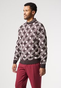 Brunmönstrad tröja med rund hals, med vita och vinröda bladliknande former, kombinerad med vinröda byxor. Strukturert stickad tyg.