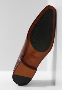 Semelle de chaussure en cuir marron à forme arrondie, avec un talon en caoutchouc noir et le nom de la marque embossé. Taille indiquée comme 41.