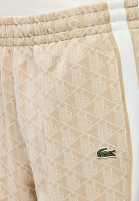 Μπεζ φόρμα με υφή γεωμετρικού μοτίβου, με λευκές ρίγες και κεντημένο πράσινο λογότυπο κροκοδείλου στο πλάι.