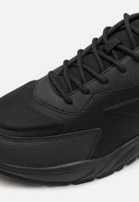 Black athletic shoe featuring a textured fabric upper, reinforced stitching, and a padded collar. Designed with a cushioned, sculpted outsole.