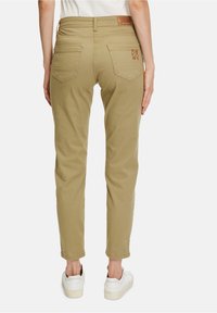 Khaki zúžené kalhoty s polovičním pasem, zadními kapsami a koženou nášivkou. Mají čistou, hladkou strukturu a zaplétaný lem.