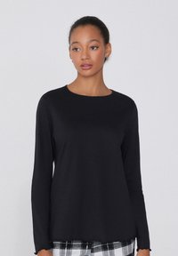 Černý top s dlouhým rukávem a kulatým výstřihem, hladkou texturou a jemně zvlněným lemem, v kombinaci s kalhotami s kostkovaným vzorem.