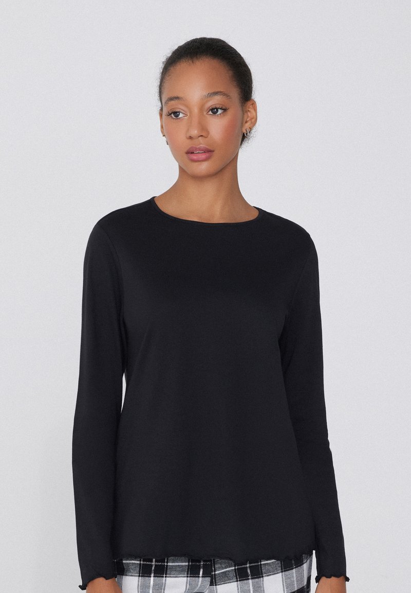 Černý top s dlouhým rukávem a kulatým výstřihem, hladkou texturou a jemně zvlněným lemem, v kombinaci s kalhotami s kostkovaným vzorem.