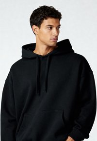 Felpa nera con cappuccio realizzata in tessuto morbido, dotata di tasca frontale, cordini e polsini a costine. Vestibilità comoda con una texture liscia.