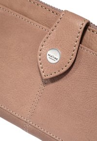 Cartera de cuero marrón claro con un acabado texturizado, costuras visibles, cierre de solapa y un detalle de botón a presión metálico grabado con "MAÎTRE."